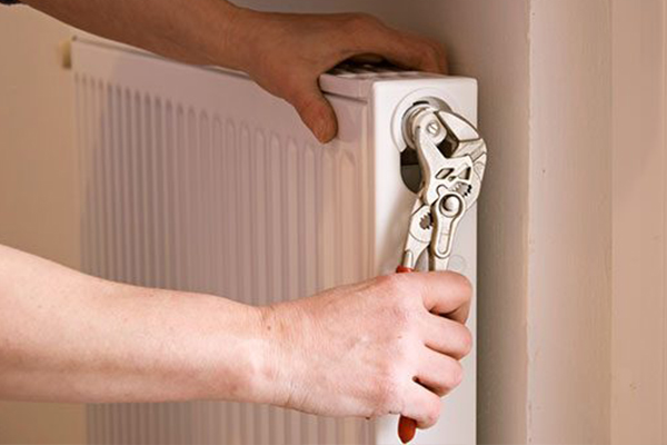 Hand with tool working on a radiator.